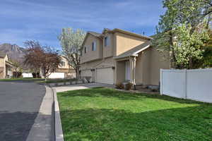 View of side of home featuring stucco siding, concrete driveway, a garage, a residential view, and roof with shingles