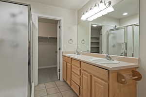 Full bathroom featuring a stall shower, a walk in closet, double vanity, and light tile patterned floors