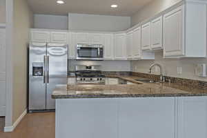 Kitchen featuring stainless steel appliances, white cabinetry, a peninsula, dark wood-style flooring, and dark stone countertops