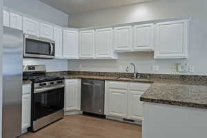 Kitchen featuring stainless steel appliances, white cabinetry, light wood-style flooring, and dark stone counters