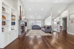 Living room featuring lofted ceiling, dark wood-type flooring, recessed lighting, and a fireplace