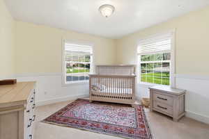 Bedroom with a crib, light colored carpet, and multiple windows