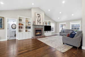 Living room with lofted ceiling, dark wood-type flooring, recessed lighting, and a brick fireplace