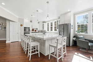 Kitchen with glass fronted cabinets, white cabinets, stainless steel appliances, a breakfast bar, and dark wood finished floors