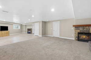 Unfurnished living room featuring a stone fireplace, light carpet, and recessed lighting