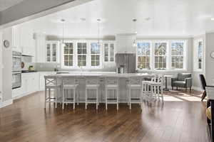 Kitchen featuring a breakfast bar, stainless steel appliances, pendant lighting, dark wood-style floors, and glass fronted cabinets