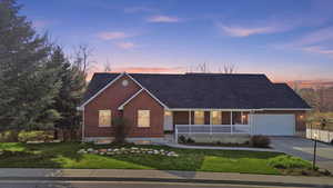 Single story home with covered porch, brick siding, concrete driveway, and a lawn