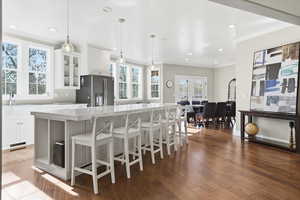 Kitchen with glass insert cabinets, white cabinets, dark wood finished floors, stainless steel refrigerator with ice dispenser, and ornamental molding