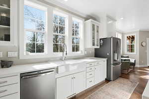 Kitchen featuring glass insert cabinets, white cabinetry, stainless steel appliances, ornamental molding, and light stone countertops
