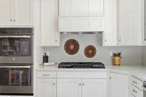 Kitchen with double oven, white cabinetry, and light stone counters