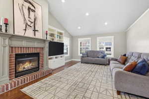 Living area featuring lofted ceiling, dark wood-style floors, plenty of natural light, a brick fireplace, and recessed lighting