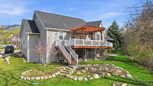 Back of house featuring roof with shingles, a wooden deck, a lawn, and a pergola
