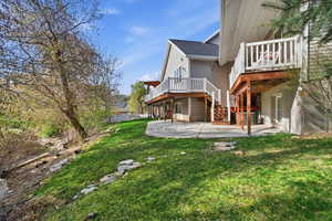 Rear view of property featuring a yard, a deck, a patio area, and roof with shingles