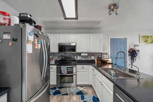 Kitchen featuring stainless steel appliances, dark countertops, white cabinetry, and tasteful backsplash