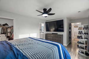 Bedroom with wood finished floors, a spacious closet, a ceiling fan, and connected bathroom