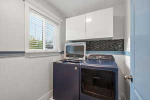Laundry room with wainscoting, washing machine and clothes dryer, and cabinet space