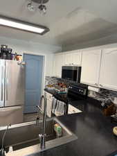 Kitchen featuring stainless steel appliances, dark countertops, white cabinetry, and decorative backsplash