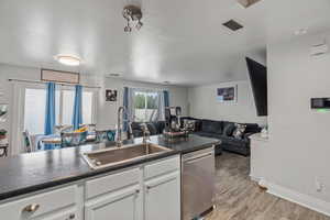 Kitchen with open floor plan, dark countertops, stainless steel dishwasher, light wood finished floors, and white cabinets