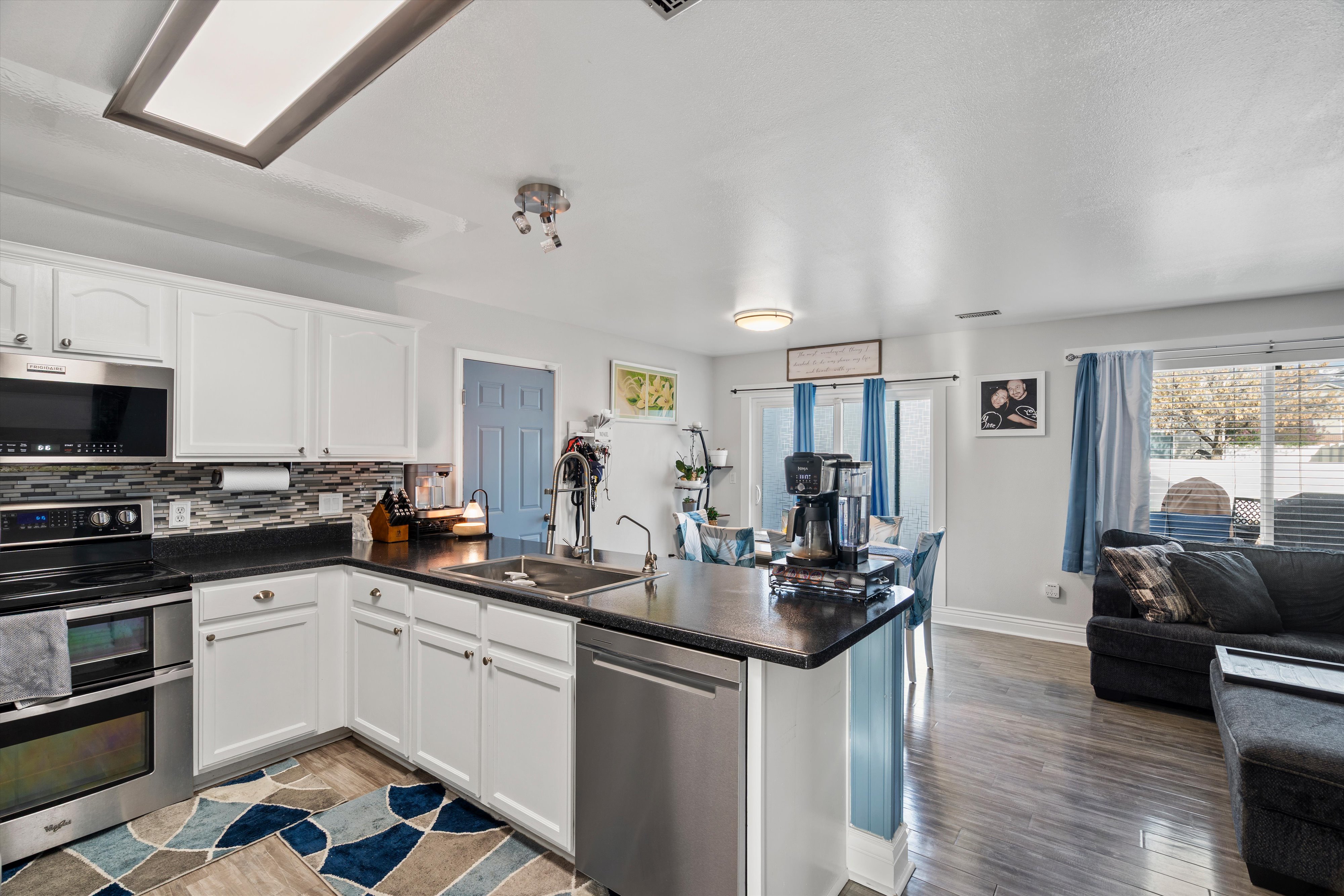 Kitchen with stainless steel appliances, dark countertops, white cabinetry, open floor plan, and a peninsula