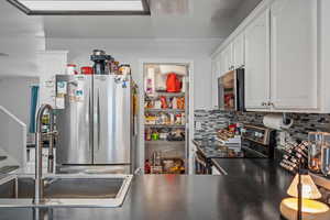 Kitchen with stainless steel appliances, dark countertops, white cabinetry, and tasteful backsplash