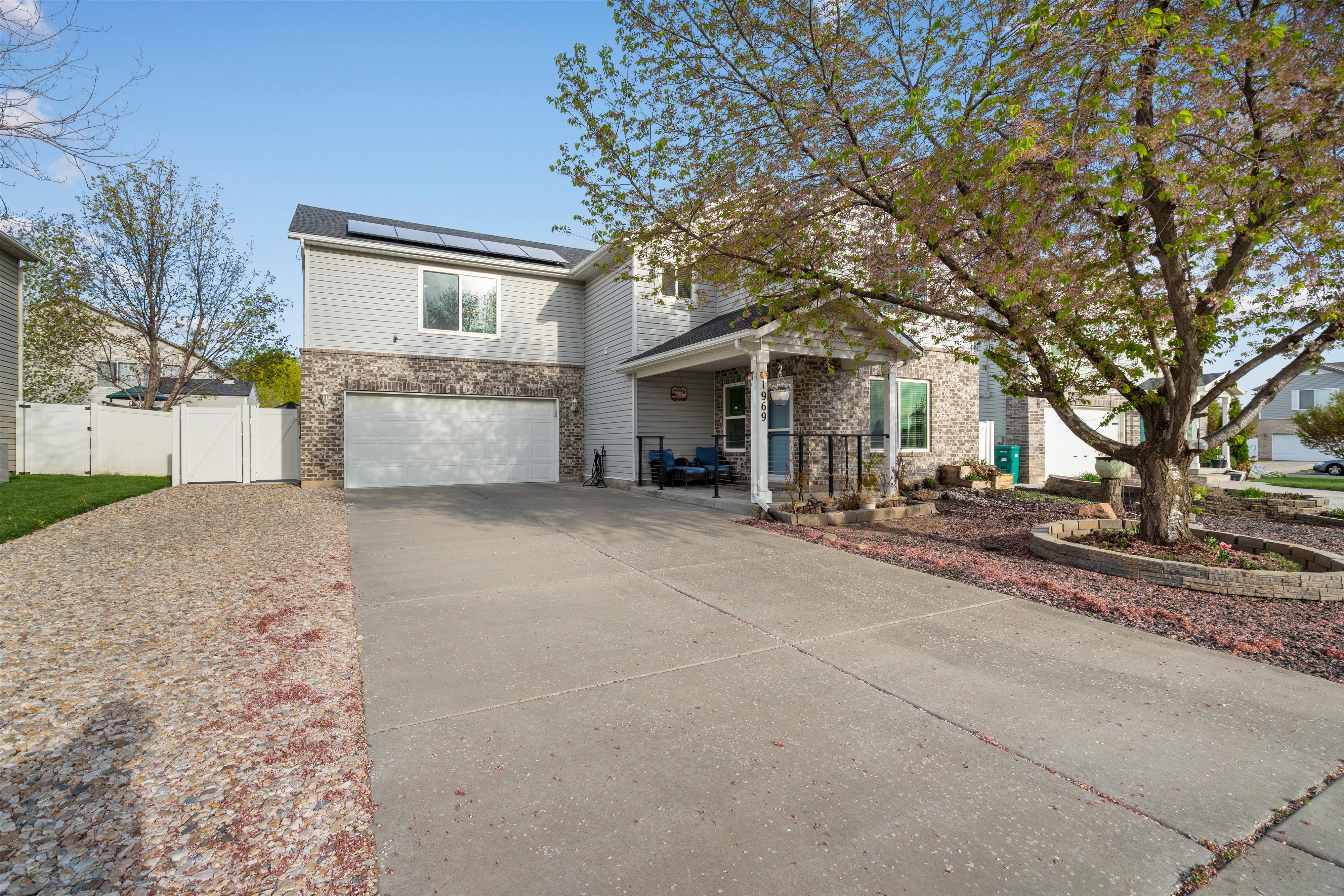 Traditional home featuring a gate, solar panels, a garage, driveway, and stone siding