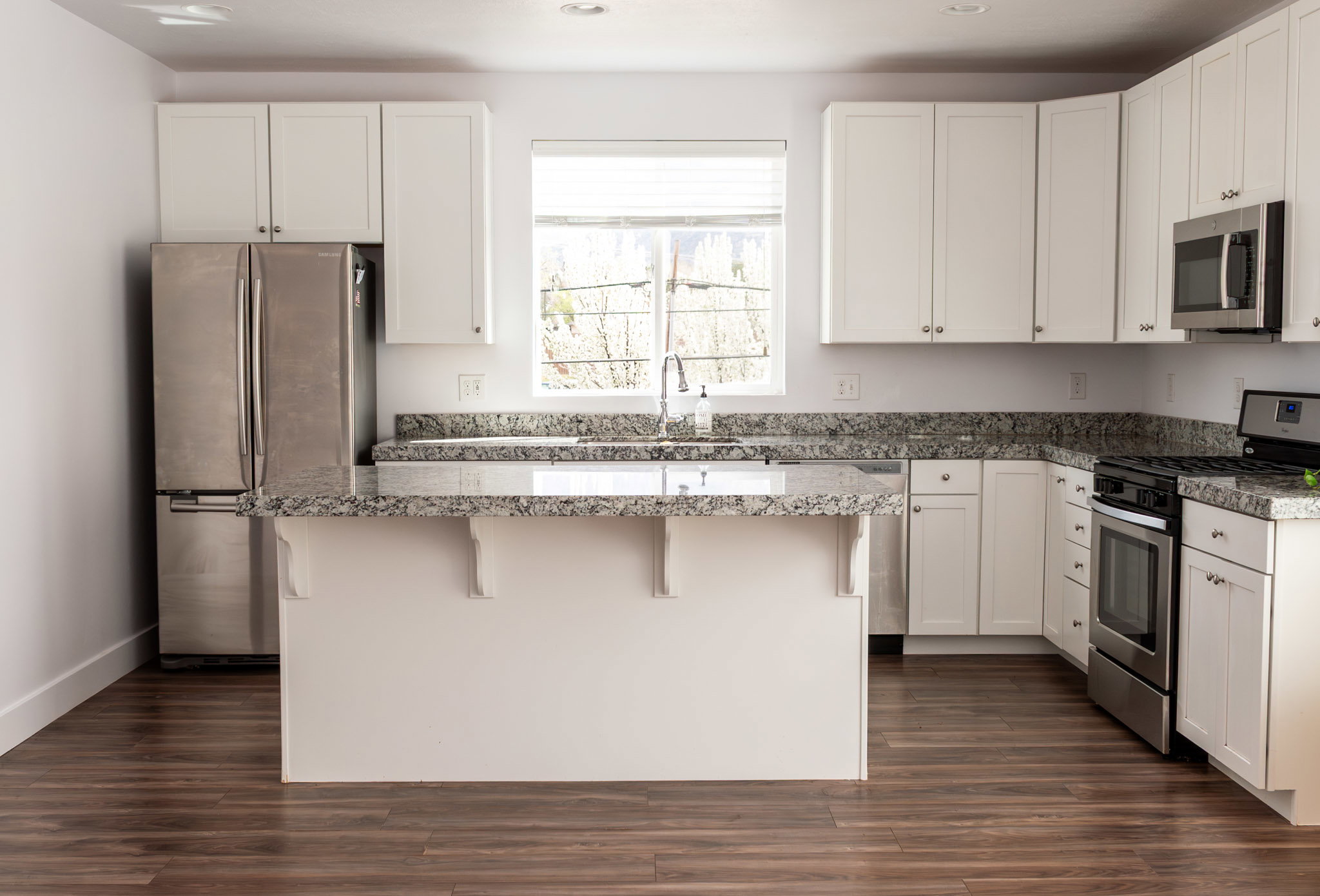 Kitchen featuring stainless steel appliances, white cabinetry, a kitchen breakfast bar, dark wood-type flooring, and a center island