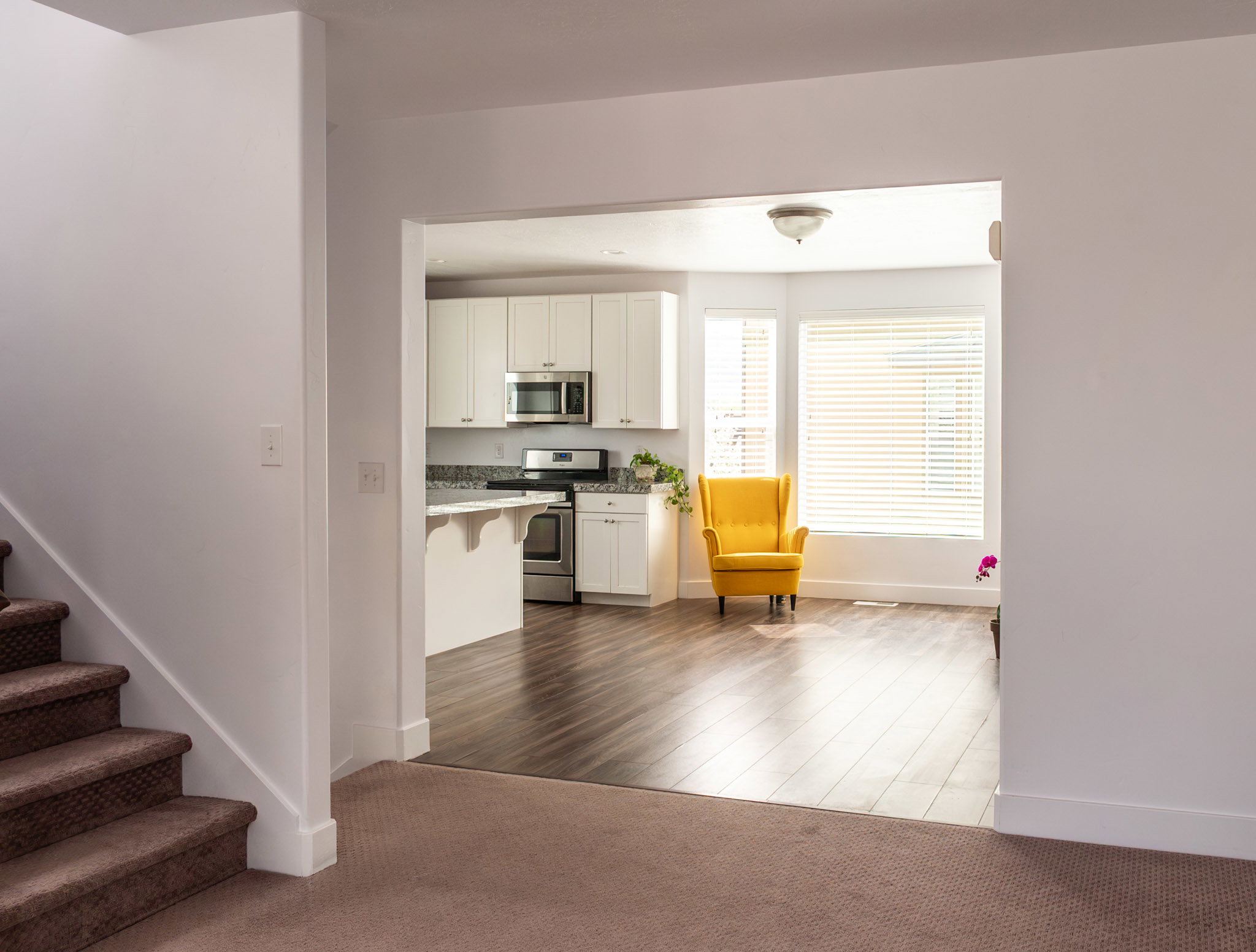Kitchen with stainless steel appliances, white cabinets, dark colored carpet, a kitchen bar, and light stone counters