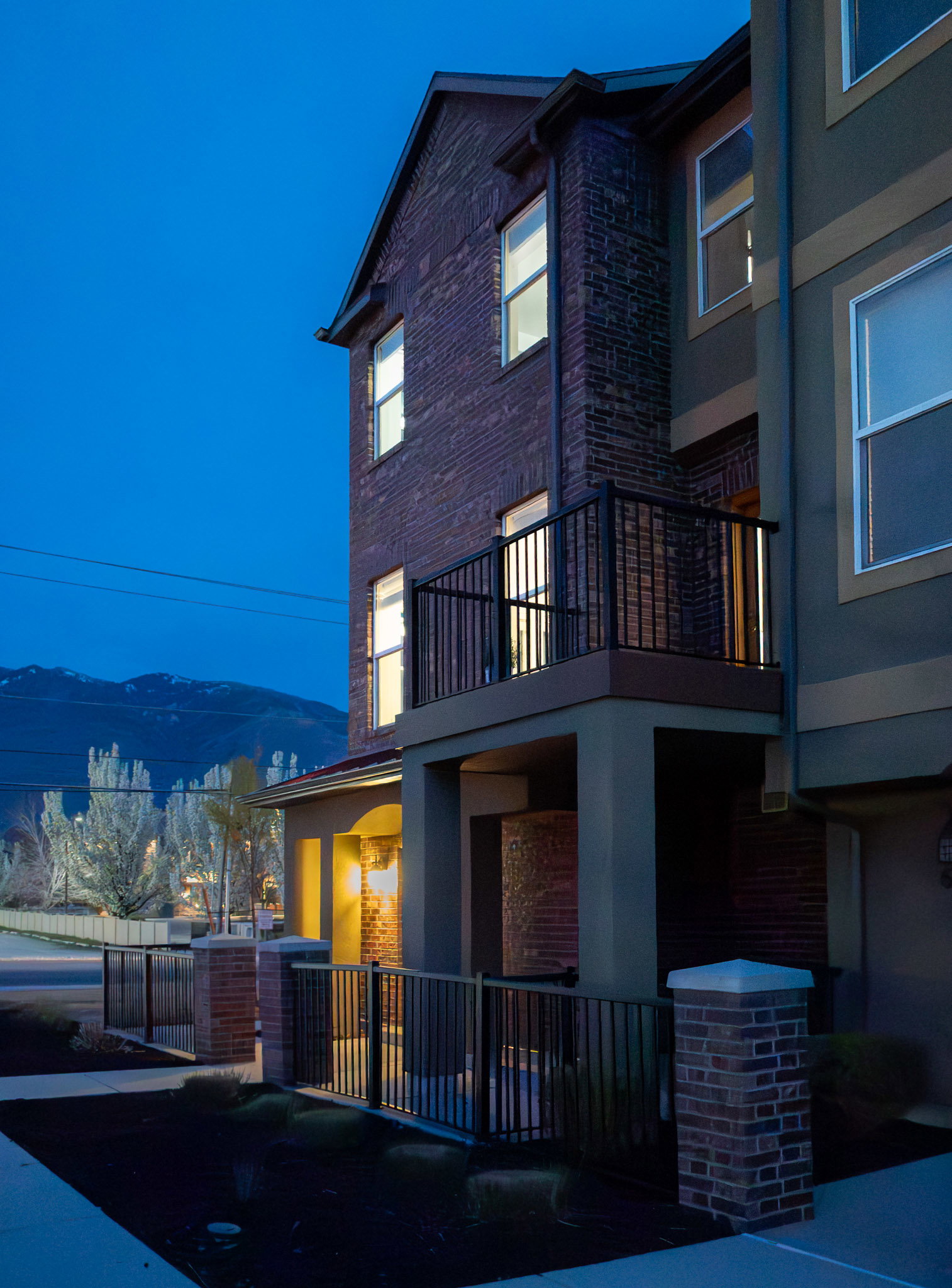 Property exterior at night featuring a mountain view, a balcony, stucco siding, brick siding, and stone siding