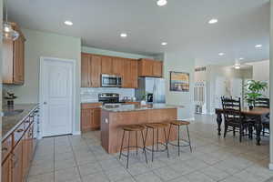 Kitchen featuring light stone countertops, a kitchen island, stainless steel appliances, wood finish cabinetry, and a breakfast bar