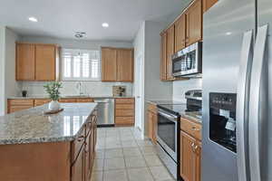 Kitchen featuring stainless steel appliances, light stone counters, decorative light fixtures, wood finish cabinets, and light tile patterned flooring