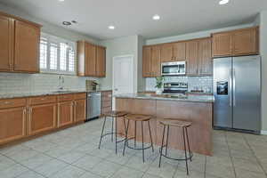 Kitchen with light stone countertops, stainless steel appliances, wood finish cabinetry, decorative light fixtures, and a kitchen island