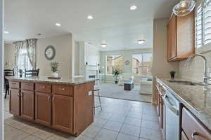 Kitchen featuring light stone counters, wood finish cabinetry, a kitchen breakfast bar, and recessed lighting