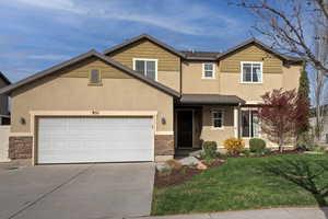 Traditional-style house featuring stone siding, driveway, a front yard, an attached garage, and covered porch