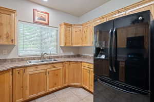 Kitchen with black refrigerator with ice dispenser, light countertops, light tile patterned floors, and light wood finish cabinetry