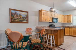Kitchen featuring a kitchen bar, a peninsula, black appliances, light wood finish cabinetry, and light tile patterned floors