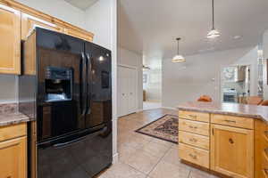 Kitchen featuring black fridge, light countertops, light tile patterned flooring, and light wood finish cabinetry
