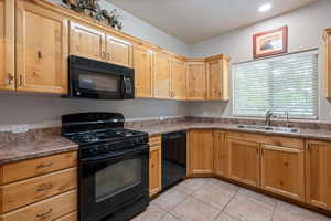 Kitchen with black appliances, light tile patterned flooring, and dark countertops
