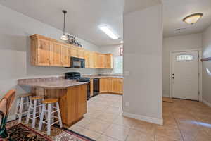 Kitchen with black appliances, a breakfast bar, a peninsula, and light wood finish cabinets