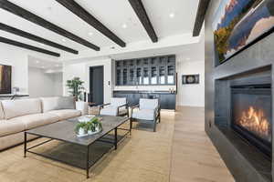 Living area featuring a glass covered fireplace, light wood-style flooring, recessed lighting, beamed ceiling, and wine cooler