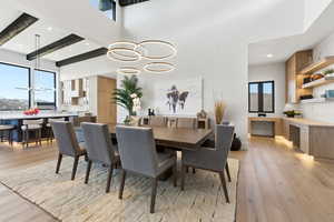 Dining room with light wood-type flooring, suspended lighting, healthy amount of natural light, and a high ceiling