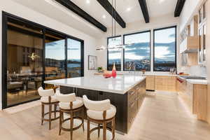 Kitchen with a spacious island, a kitchen bar, light stone countertops, hanging lights, and glass fronted cabinets