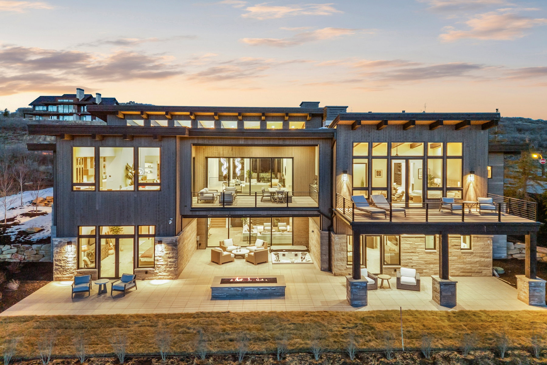 Back of house at dusk with an outdoor living space with a fire pit, stone siding, a patio area, and a balcony