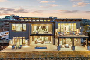 Back of house at dusk with an outdoor living space with a fire pit, stone siding, a patio area, and a balcony