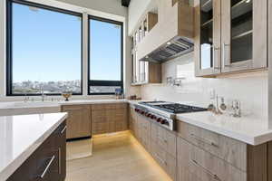 Dual tone kitchen featuring light stone counters, stainless steel gas stovetop, light wood-style floors, glass insert cabinets, and modern cabinets