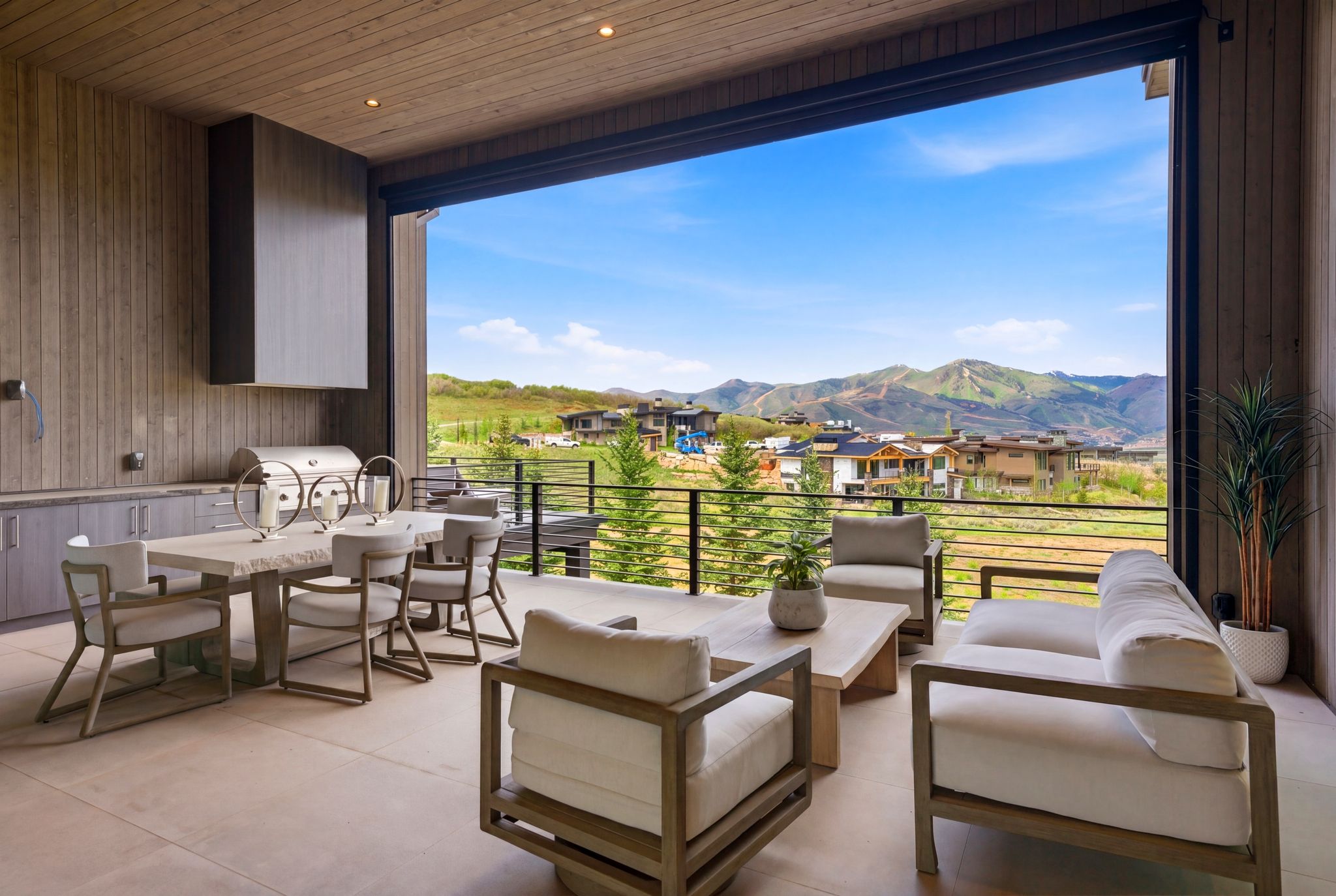 Expansive outdoor patio featuring an integrated built-in grill, custom cabinetry, a stone-finish dining table, and a protective overhang with recessed lighting
