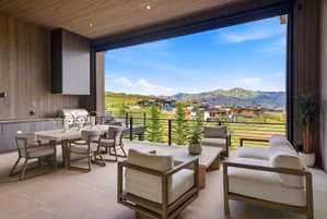 Expansive outdoor patio featuring an integrated built-in grill, custom cabinetry, a stone-finish dining table, and a protective overhang with recessed lighting