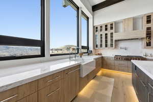 Dual tone kitchen with light wood finished floors, light stone counters, stainless steel gas stovetop, glass fronted cabinets, and dual tone cabinets