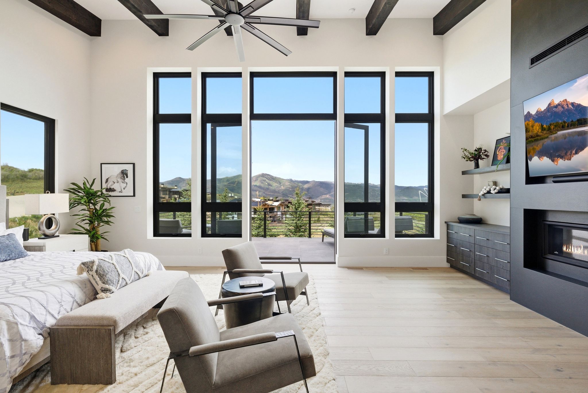 Vaulted ceiling with exposed wood beams, expansive floor-to-ceiling windows, built-in media center with integrated fireplace, light wood-finish flooring, and a large outdoor patio
