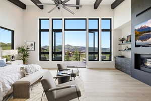 Vaulted ceiling with exposed wood beams, expansive floor-to-ceiling windows, built-in media center with integrated fireplace, light wood-finish flooring, and a large outdoor patio