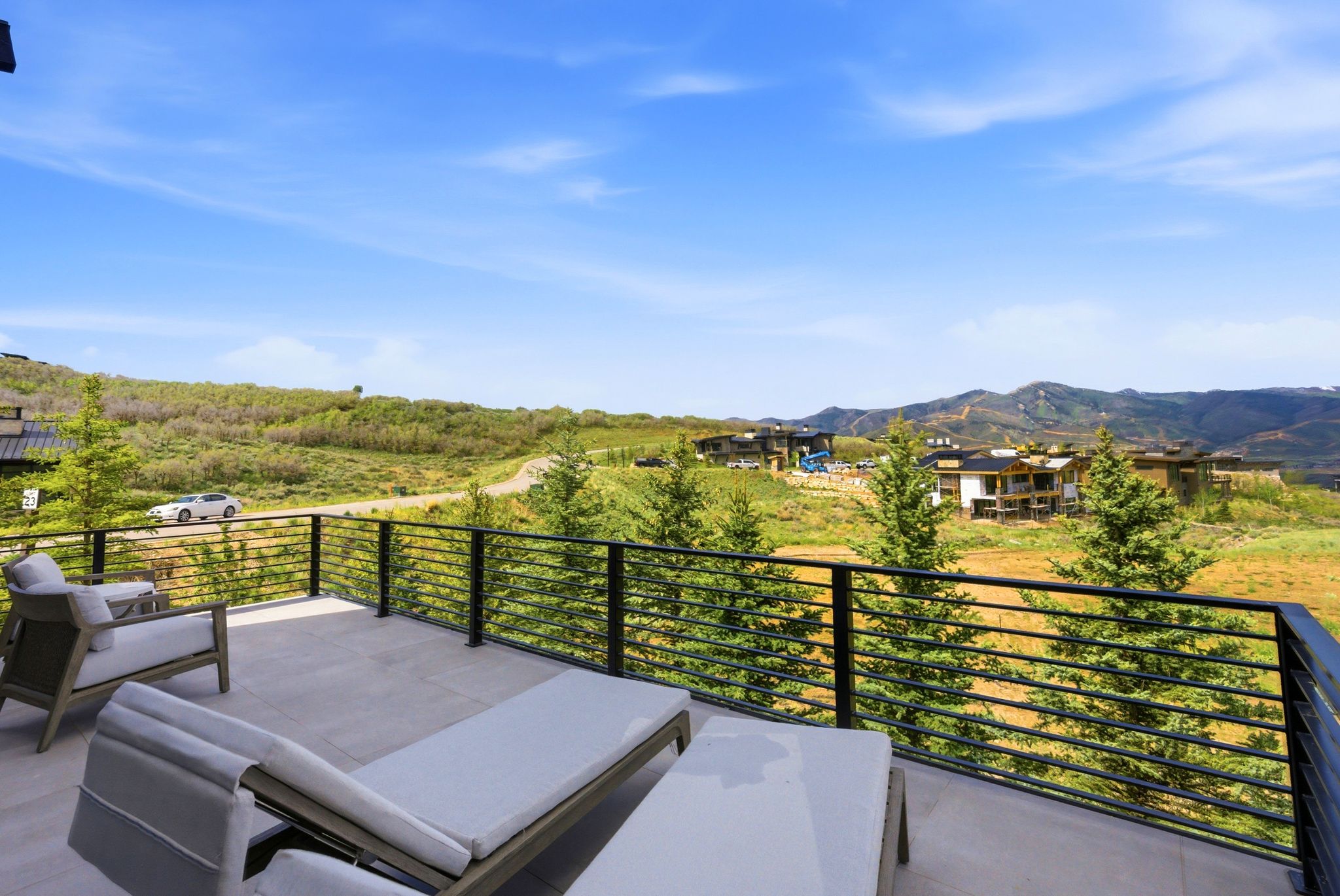 Outdoor terrace with neutral-toned tile flooring, black horizontal bar railings, and a mountainous backdrop